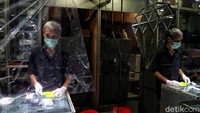 Seorang pedagang reprasi perhiasan membuka tokonya dengan prokol kesehatan dengan menyekat kiosnya dengan plastik dan mengunkan masker.