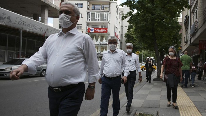 A woman watches the men wearing face masks for protection against the coronavirus and respecting social distance, in popular Tunali Hilmi Street, in Ankara, Turkey, Wednesday, May 27, 2020. Turkish children under 14 were allowed to go out between 12:00-15:00 local time for the third time. (AP Photo/Burhan Ozbilici)