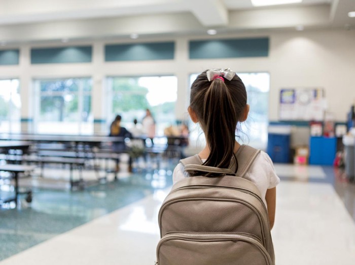 Elementary schoolgirl enters the school cafeteria. She pauses while looking for a friend.