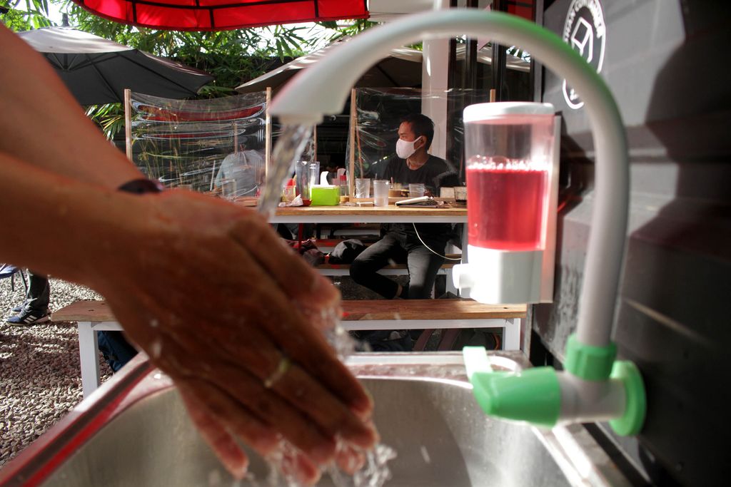 Pelayan memasang poster imbauan kepada pengunjung di pintu masuk salah satu warung kopi di Makassar, Sulawesi Selatan, Jumat (29/5/2020). Warung kopi yang mulai melayani pengunjung  pascapenerapan Pembatasan Sosial Berskala Besar (PSBB) di daerah itu tersebut menerapkan protokol kesehatan sesuai serat edaran yang diterbitkan Kementerian Kesehatan pada 20 Mei 2020 terkait protokol pencegahan penularan virus Corona untuk mendukung keberlangsungan usaha dan perekonomian masyarakat. ANTARA FOTO/Arnas Padda/yu/wsj.