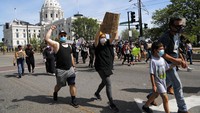 Seorang anak terlihat di antara massa pendemo di St Paul. Dengan mengenakan kaos dan celana pendek, dia tampak digandeng peserta aksi lainnya. AP Photo/Julio Cortez.