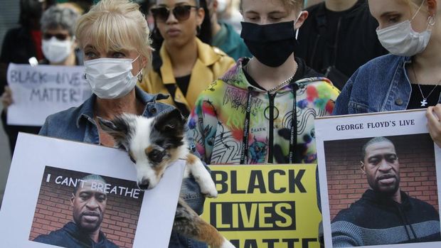 People wearing face masks stand at a protest and hold pictures of George Floyd and signs reading 