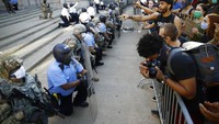 Polisi dan tentara berlutut di depan demonstran yang menggelar aksi di dekat markas Kepolisian Philadelphia. AP Photo/Matt Rourke.