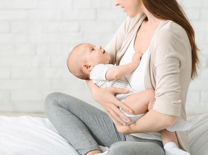 Closeup of young woman holding cute little baby in her hands, lulling him in bed. Panorama with free space