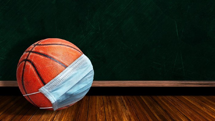 Basketball wearing surgical mask on a background chalk board with copy space for text. Concept of COVID-19 coronavirus pandemic affecting basketball seasons due to game or league suspensions or cancellations.