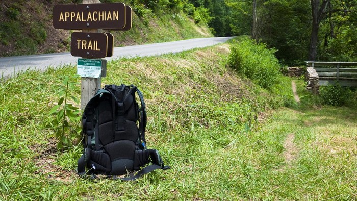 A backpackers pack rest against a signpost for the Appalachian Trail in southwest Virginia. The road is state route 650, several miles from Marion, VA. The trail crosses the road and goes across the footbridge seen on the right.