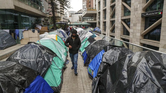 A Bolivian migrant pases a box milk while others in line up for a free lunch at a camp outside the Bolivian consulate to demand repatriation, amid the spread of the new coronavirus and lack of work in Santiago, Chile, June, Tuesday, 2, 2020. Citizens of Peru, Bolivia, Venezuela and Colombia living in Chile are camping in front of their respective consulates to demand that they help them to return home. (AP Photo/Esteban Felix)