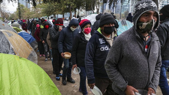 A Bolivian migrant pases a box milk while others in line up for a free lunch at a camp outside the Bolivian consulate to demand repatriation, amid the spread of the new coronavirus and lack of work in Santiago, Chile, June, Tuesday, 2, 2020. Citizens of Peru, Bolivia, Venezuela and Colombia living in Chile are camping in front of their respective consulates to demand that they help them to return home. (AP Photo/Esteban Felix)