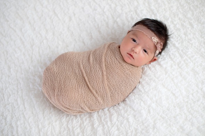 One month old baby girl swaddled in a beige wrap. Shot in the studio on a white blanket.