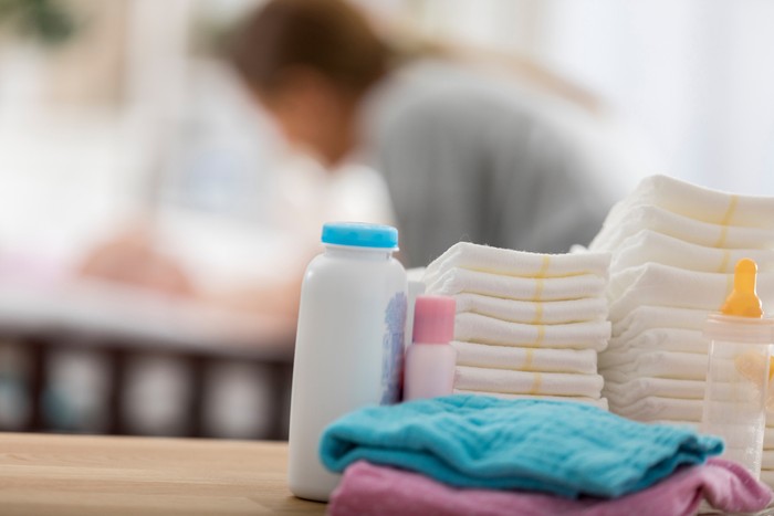 859936614 Close up of baby products sitting on a table in a babys nursery. A mom is changing a babys diaper in the background.