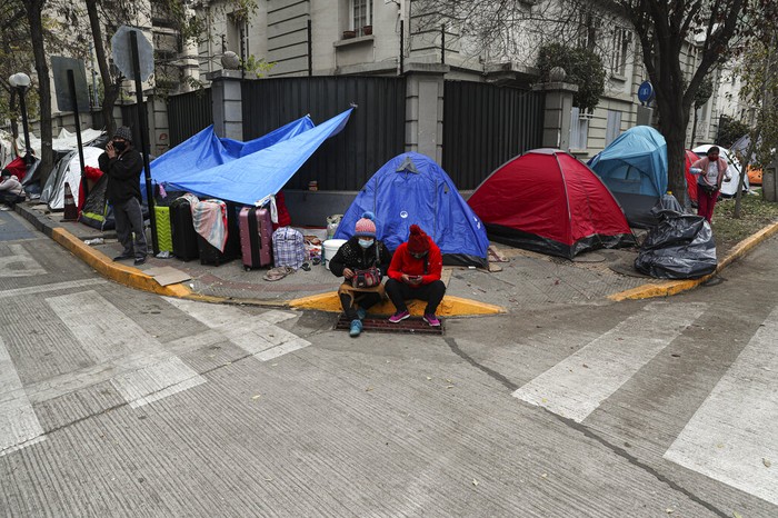Migran di Chili Kemah Tuntut Repatriasi A Bolivian migrant pases a box milk while others in line up for a free lunch at a camp outside the Bolivian consulate to demand repatriation, amid the spread of the new coronavirus and lack of work in Santiago, Chile, June, Tuesday, 2, 2020. Citizens of Peru, Bolivia, Venezuela and Colombia living in Chile are camping in front of their respective consulates to demand that they help them to return home. (AP Photo/Esteban Felix)