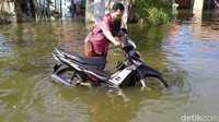 Seorang warga mendorong sepeda motornya yang mogok akibat menerobos banjir.