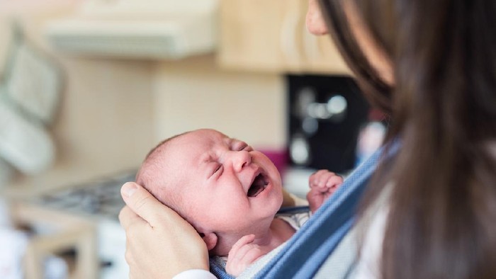Ilustrasi bayi menangis Close up of unrecognizable young mother with her crying newborn baby son in sling at home