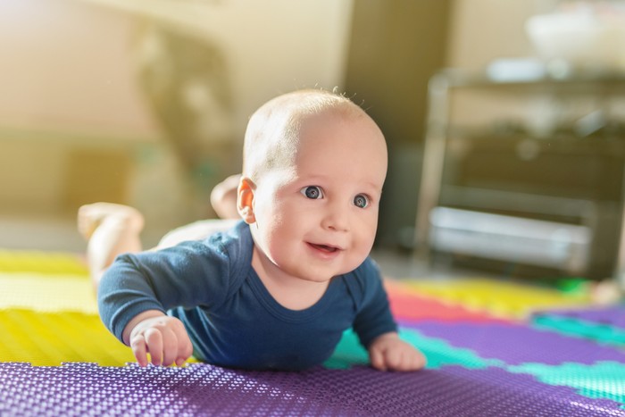Portrait of cute caucasian baby boy crawling on soft playing mat indoors. Adorable child having fun making making first steps on floor at nursery. Backlit.  Happy childhood and evolution concept.