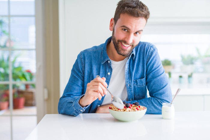 Handsome man having breakfast eating cereals at home and smiling