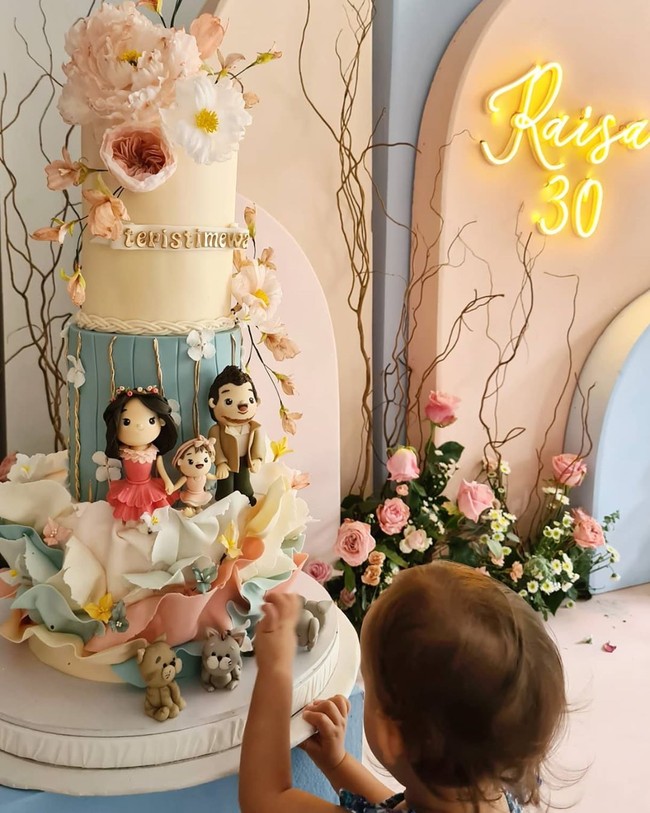 Acara ulang tahun kurang lengkap tanpa kehadiran kue ulang tahun. Tidak tanggung-tanggung ada dua kue ulang tahun untuk Raisa. Kue pertama bertingkat tinggi, dipermanis dengan dekorasi bernuansa floral serta hiasan yang merepresentasikan Raisa, Hamish dan putri mereka, Zalina.  KalimatTeristimewa ikut menghiasi kue tersebut. Tampak Zalina sudah tak sabar untuk menikmatinya. (Foto: Instagram/@hamishdw)