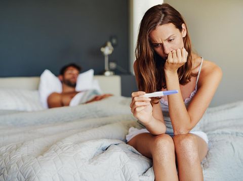 Test pack Shot of a woman looking worried while holding a pregnancy test with her partner lying in the background