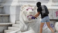 Seorang demonstran menghancurkan patung singa dengan palu.