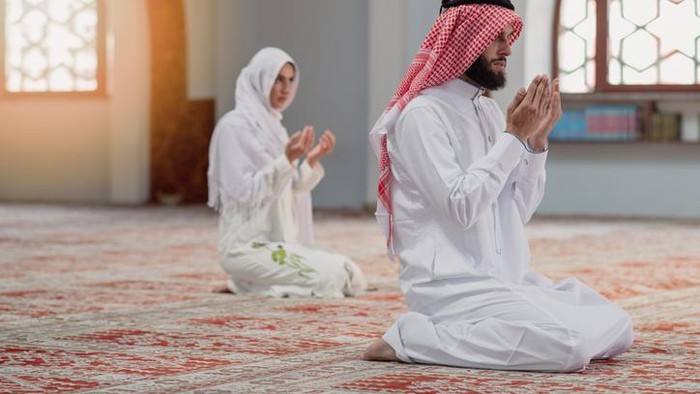 Muslim man and woman praying for Allah in the mosque together.