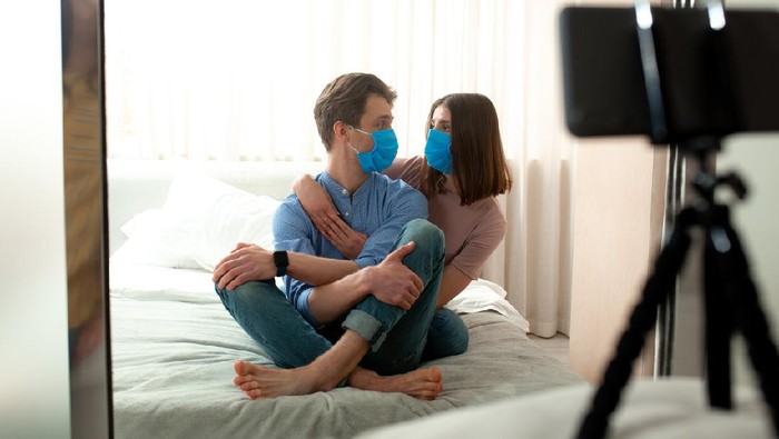 pasutri pakai masker saat bercinta Young male and female in blue protective masks taking photo by phone on tripod at home