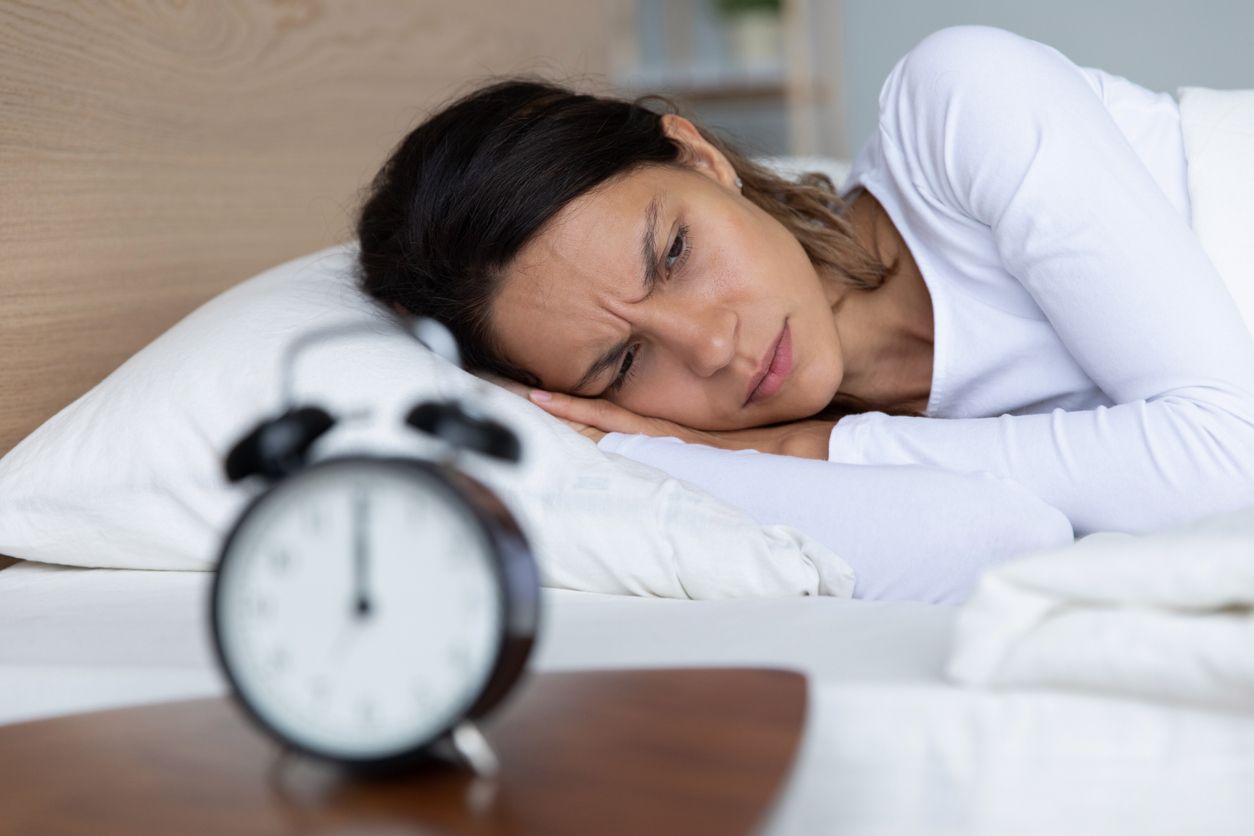 Unhappy restless woman wearing pajama suffering from insomnia, alarm clock on bedside table, sleepless tired girl with open eyes lying in bed, lack of sleep, early morning awakening concept