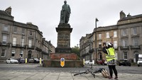Seorang warga mengambil foto patung Robert Viscount Melville yang menjadi sasaran aksi vandalisme di kawasan Edinburgh, Skotlandia, pada Rabu (10/6/2020) waktu setempat. Patung itu menjadi sasaran aksi vandalisme karena dianggap menjadi salah satu tokoh yang pro-kolonial dan perbudakan. Andrew Milligan/PA via AP.