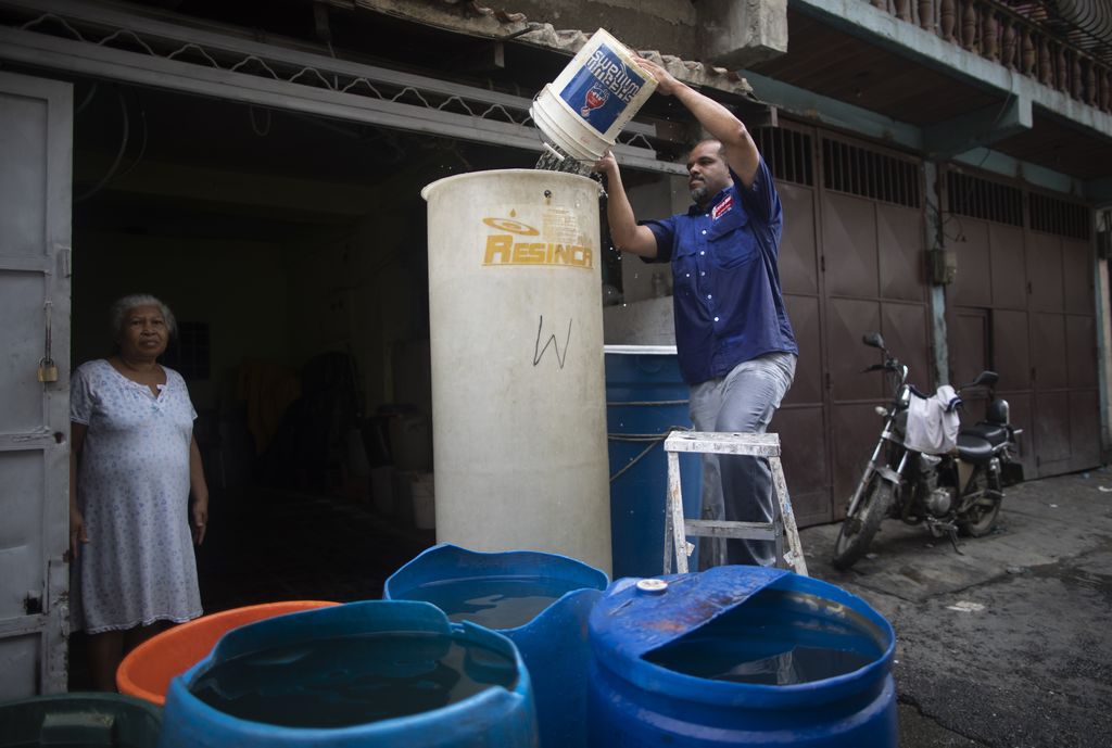 A resident fills a tall container with water provided by a government water truck, in the Petare slum of Caracas, Venezuela, Wednesday, June 10, 2020. Amid water shortages during the COVID-19 pandemic, the government is providing free water to some areas. (AP Photo/Ariana Cubillos)