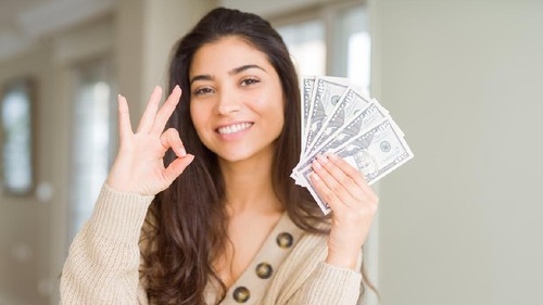 Young woman holding 50 dollars bank notes doing ok sign with fingers, excellent symbol