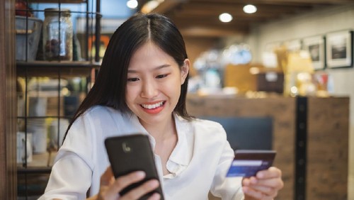 Young woman holding 50 dollars bank notes doing ok sign with fingers, excellent symbol