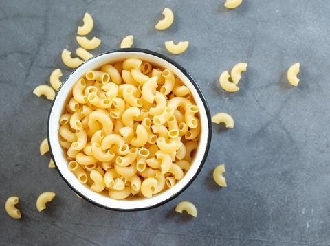 raw elbow macaroni in enamel bowl on dark cement table background.