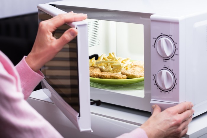 928066216 Unhappy Young Woman Looking At Smoke Emitting Through Microwave Oven In Kitchen