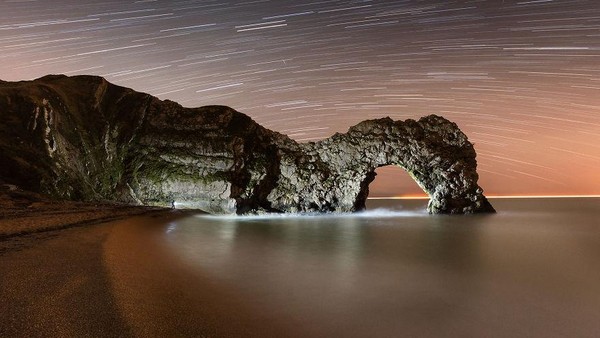 Foto komposit ini menunjukkan pantai yang gelap dan kosong di samping Durdle Door di Pantai Jurassic Dorset, dengan sekitar satu jam rotasi bumi direkam dalam jejak bintang di langit. Jika diperhatikan dengan teliti, Anda mungkin dapat melihat sosok mungil yang sedang menerangi wajah batu dari garis pantai. Foto komposit ini menunjukkan pantai yang gelap dan kosong di samping Durdle Door di Pantai Jurassic Dorset, dengan sekitar satu jam rotasi bumi direkam dalam jejak bintang di langit. Jika diperhatikan dengan teliti, Anda mungkin dapat melihat sosok mungil yang sedang menerangi wajah batu dari garis pantai.