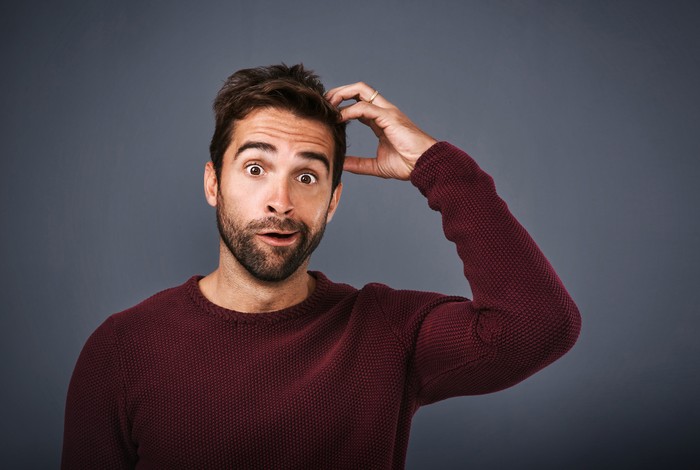 Studio shot of a young man scratching his head in confusion against a gray background