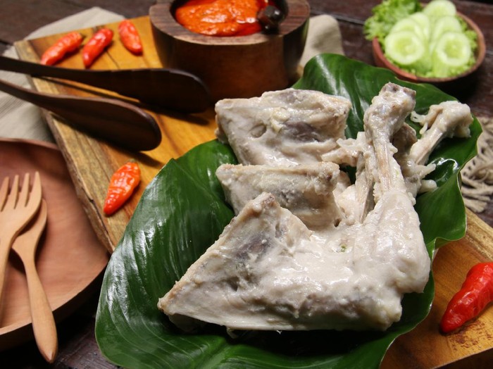 Ilustrasi ayam pop Ayam Pop, a popular chicken dish from Minangkabau, Padang, West Sumatra. The chicken is braised in coconut milk and spices; then only lightly fried. It is served with a special spicy paste of red chili peppers, tomatoes, and broad beans. The chicken pieces are arranged on rectangular wooden serving block that has been lined with a broad green leaf. On the other end is the chili paste. Some chili peppers are scattered on the tray. Some green vegetables of cassava leaves, lettuce and cucumber slices are also served along the chicken dish. A wooden plate with two matching wooden cutleries are placed next to the tray.