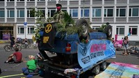 Mobil berwarna biru tersebut tampak terbalik dan dihiasi dengan sejumlah tumbuhan serta spanduk-spanduk untuk mendorong tindakan memperlambat pemanasan global.
