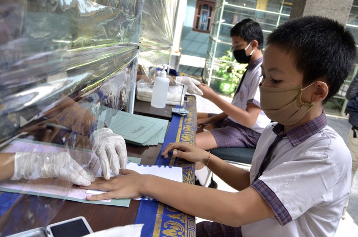 PROTOKOL KESEHATAN SAAT PENGAMBILAN DOKUMEN KELULUSAN Siswa kelas VI melakukan cap tiga jari saat proses pengambilan dokumen kelulusan di SD Widiatmika, Jimbaran, Badung, Bali, Kamis (18/6/2020). Pengambilan dokumen kelulusan berupa Surat Keterangan Lulus dan Surat Keterangan Hasil Ujian Sekolah yang mengharuskan kehadiran siswa ke sekolah untuk melakukan cap tiga jari tersebut menerapkan berbagai protokol kesehatan seperti pemeriksaan suhu tubuh dan penggunaan hand sanitizer bagi siswa dan orang tua, penggunaan alat pelindung diri bagi guru dan karyawan serta pemasangan pembatas plastik yang membatasi jarak guru dan siswa untuk mencegah penyebaran COVID-19. ANTARA FOTO/Fikri Yusuf/aww.