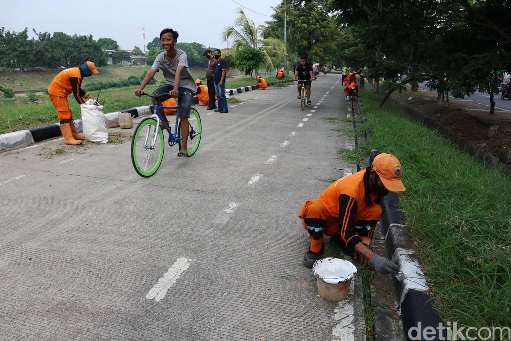 Petugas melakukan pengecetan pada pembatas jalan dan memotong rumput di Kanal Banjir Timur, Malaka Jaya, Jumat (19/6/2020). Hal ini guna memberikan kenyamanan pada warga yang berolahraga dikawasan tersebut.