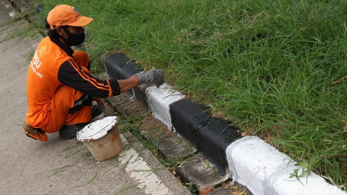 Aksi Pasukan Oranye Percantik Jalan Inspeksi KBT Petugas melakukan pengecetan pada pembatas jalan dan memotong rumput di Kanal Banjir Timur, Malaka Jaya, Jumat (19/6/2020). Hal ini guna memberikan kenyamanan pada warga yang berolahraga dikawasan tersebut.