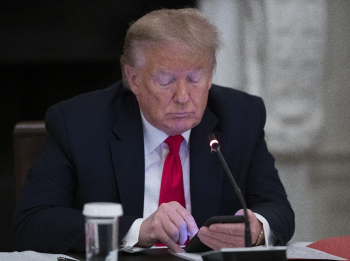 President Donald Trump looks at his phone during a roundtable with governors on the reopening of Americas small businesses, in the State Dining Room of the White House, Thursday, June 18, 2020, in Washington. (AP Photo/Alex Brandon)