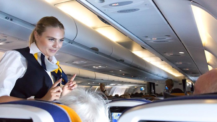 Munich: A female flight attendant  is speaking with a passenger sitting in the economy class of the route Munich - Vancouver of Lufthansa Airlines.