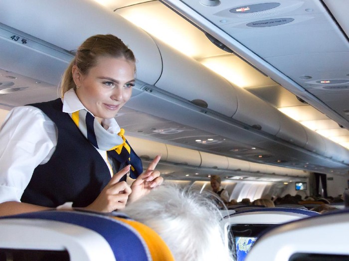 Ilustrasi pramugari Munich: A female flight attendant is speaking with a passenger sitting in the economy class of the route Munich - Vancouver of Lufthansa Airlines.