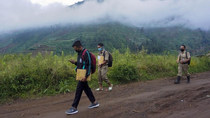 Kepala Sekolah SMP N 4 Bawang Mulud Sugito (tengah) dan guru Wiyata Bhakti bersiap melewati aliran sungai di dasar bukit saat mengantar lembar tugas siswa secara langsung ke rumahnya di Pranten, Kecamatan Bawang, Kabupaten Batang, Jawa Tengah.