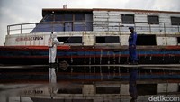 Seorang petugas sedang menyemprotkan cairan disinfektan ke bagian luar kapal nelayan tradisional yang berada di kawasan Pelabuhan Kali Adem, Jakarta, Jumat (19/6/2020).