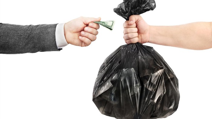 The concept of recycling. A male hand in a jacket transfers money to the other hand in exchange for a garbage bag.