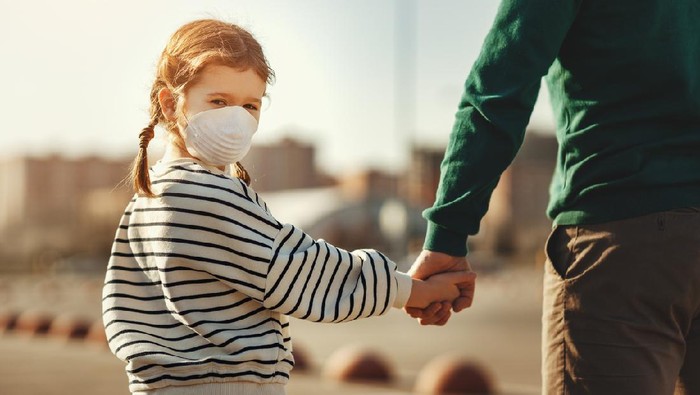 Anak menggunakan masker Little boy in medical mask hugging crop mother and looking at camera during coronavirus outbreak against gray background