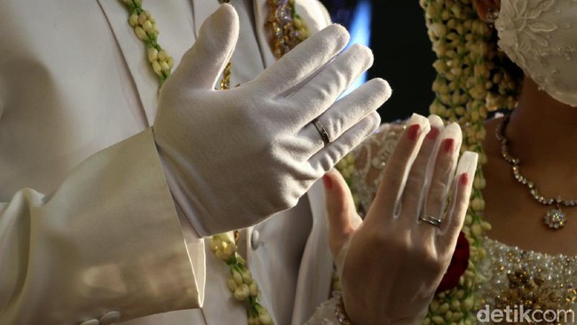 Pelaksanaan pernikahan di era new normal itu membuat pengantin memakai cincin kawin di atas sarung tangan.