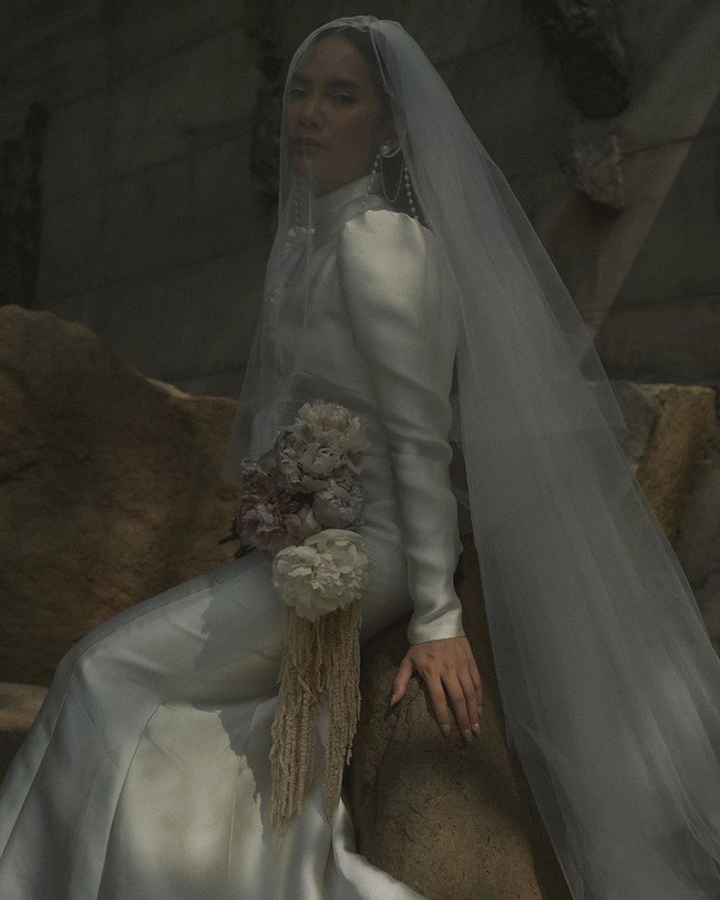 Gaun bernuansa vintage menjadi pilihan Tara Basro ketika meresmikan hubungannya dengan Daniel Adnan. Gaun berwarna off-white tersebut berlengan panjang dan memiliki kerah tinggi. Penampilan Tara Basro kian maksimal dengan veil panjang yang menjuntai sampai menyentuh lantai. Tidak ketinggalan, anting bergaya klasik yang terbuat dari susunan mutiara. (Foto: Instagram/@tarabasro)