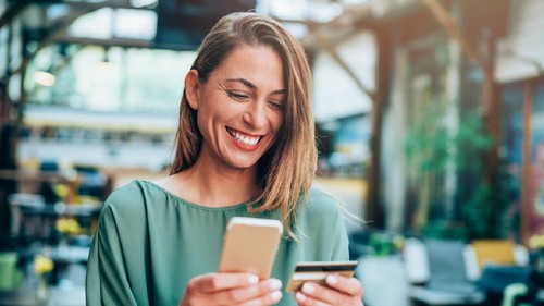 Young woman sitting in a cafe and holding credit card and smart phone