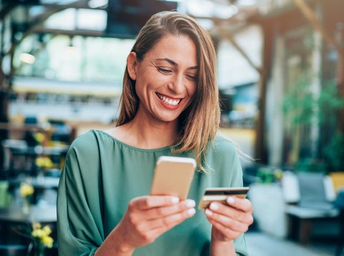 Young woman sitting in a cafe and holding credit card and smart phone