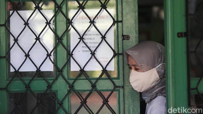 Guru membagikan laporan hasil belajar (rapor) kenaikan kelas kepada wali murid di SD Negeri Menteng 01, Jakarta, Kamis (25/6/2020). Pembagian rapor akhir tahun pelajaran 2019/2020 dilaksanakan mengikuti protokol kesehatan pencegahan penularan COVID-19 dengan menjaga jarak, mengenakan masker, pengukuran suhu tubuh serta melakukan pembagian rapor secara bertahap dari 24-26 Juni 2020.